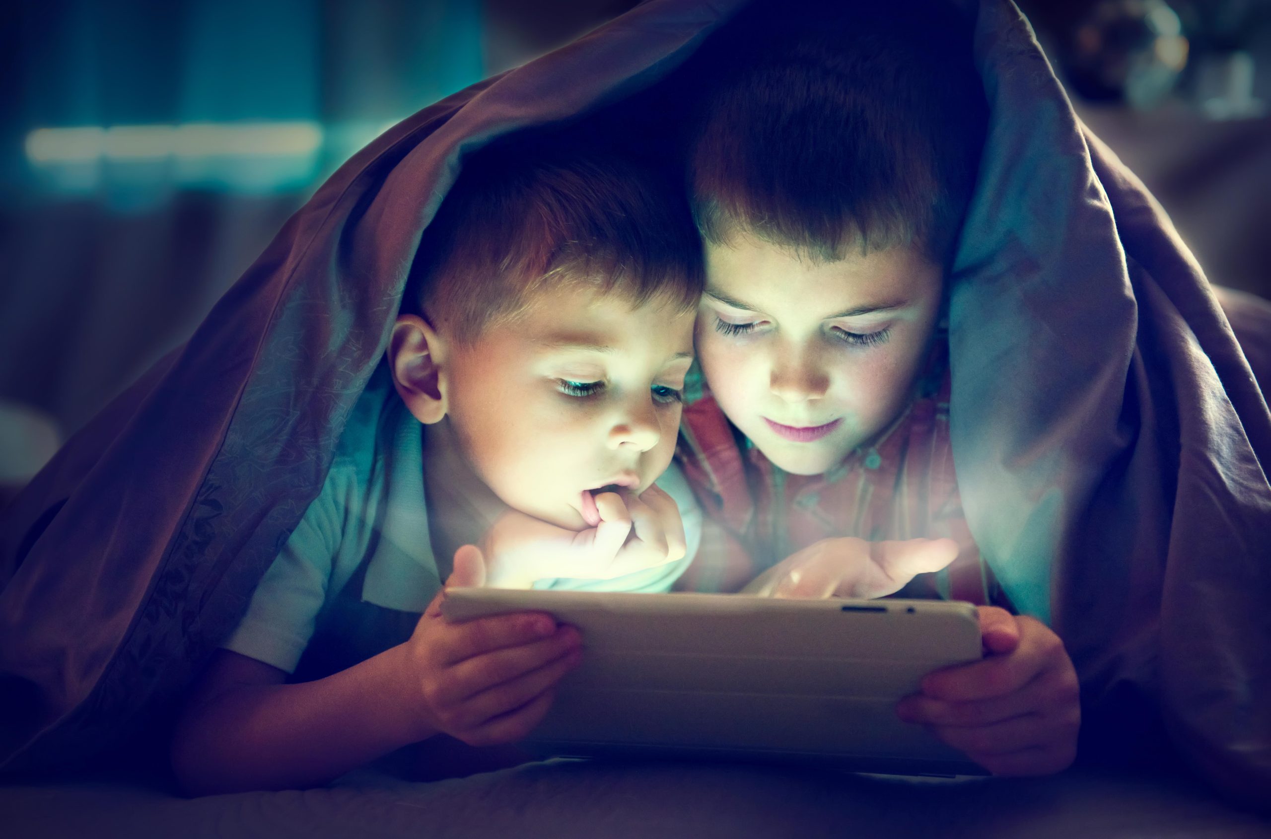 Two,Kids,Using,Tablet,Pc,Under,Blanket,At,Night.,Brothers